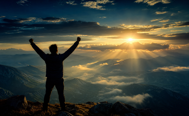A person standing on a mountaintop with arms raised celebrating freedom after completing a debt management plan.
