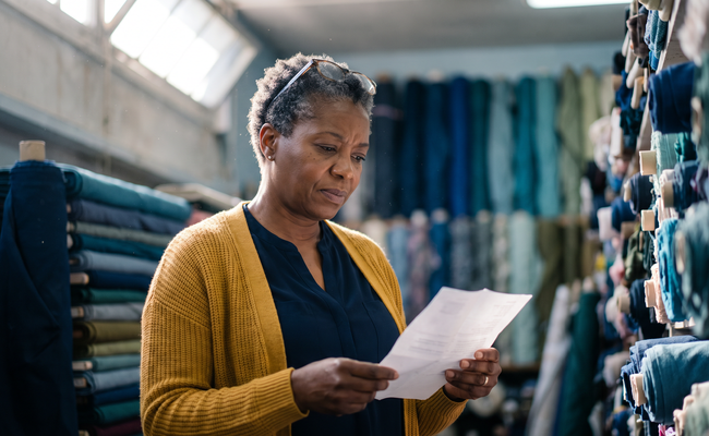 A woman in a fabric store reads a notice showing debt collector interest and fees she never agreed to pay.