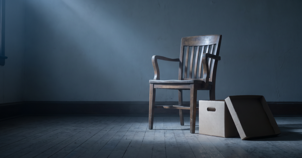 An empty wooden witness chair in a shaft of cold light, showing the seat a judgment debtor examination requires you to fill.