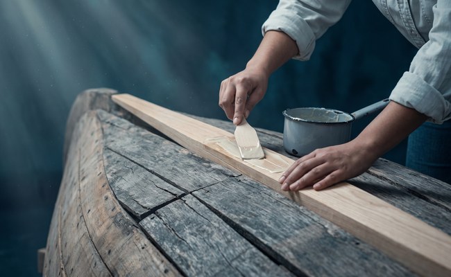 A tapered scarf joint of pale new timber is fitted into an older grey plank, the repair clearly visible.

