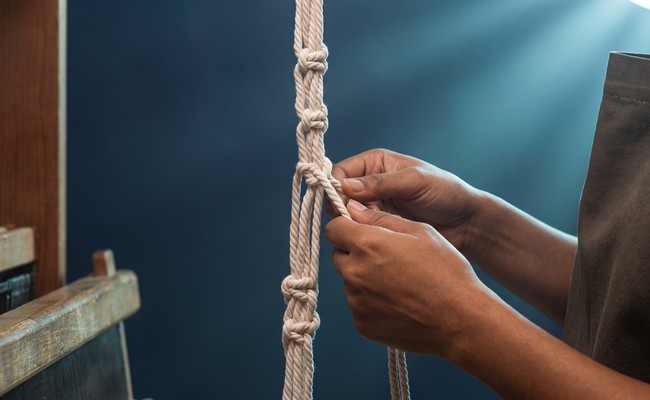 A hand ties another knot in a counting cord that already carries a row of evenly spaced knots.