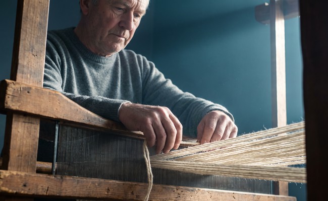 A weaver threads a fresh warp through a loom to begin the next piece of work.