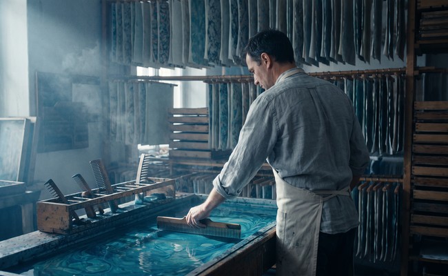 A craftsman drawing a comb through floating pigment on a marbling trough
