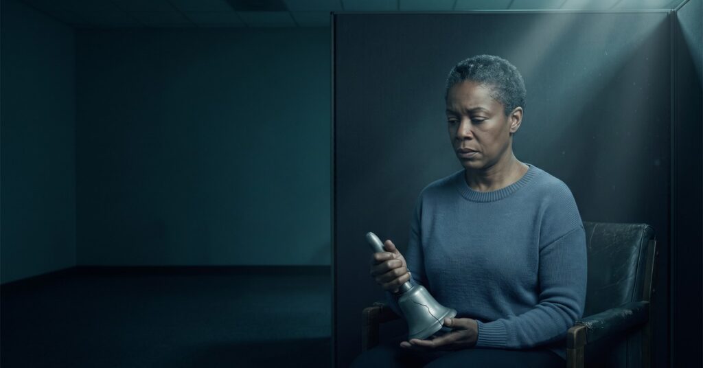 A woman sits in a bare office holding a cracked metal bell wondering if her utility bills affect credit score.