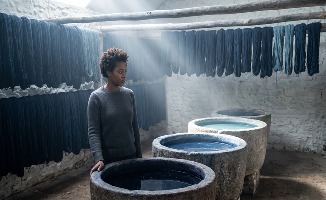 A woman stands before three stone vats holding indigo at three different strengths, looking from one to the next.