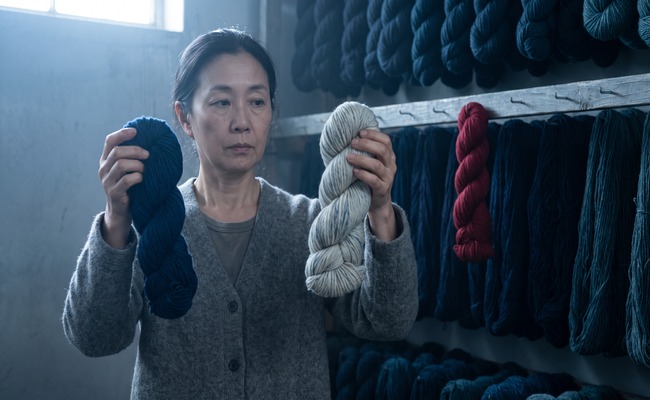 A woman holds up two skeins side by side, one dyed deep navy and one that barely took the color, comparing the difference.
