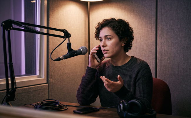 A person makes a careful issuer phone call in a community radio booth while asking about payment help.