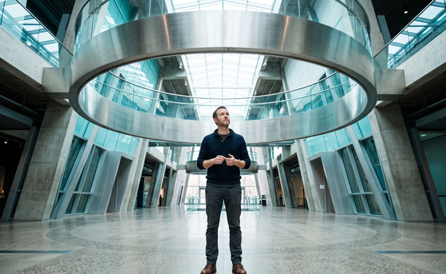 A person stands beneath a circular science-museum structure while considering the separate effects of a missed payment.