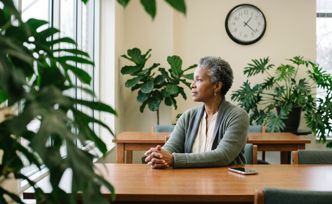 A person sits thoughtfully in a plant-filled library alcove while monitoring a credit-account question.