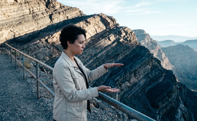 A person considers separate payment consequences beside a quarry overlook and an unmarked safety rail.
