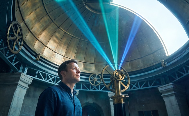 A person studies converging colored light beams representing priority in credit card payment allocation beneath an observatory dome.