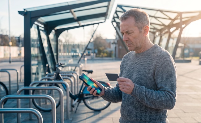 A person checks an abstract phone beside bicycle racks after an account change while holding a plain card.