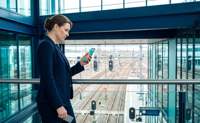A person studies an abstract phone beside railway signals while considering whether a closed account was reported accurately.