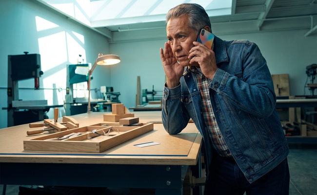 A person listens through a verified phone channel in a bright makerspace while protecting account security.
