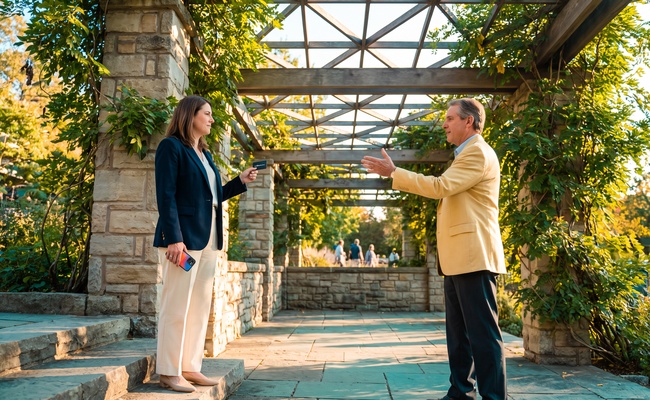 Two adults discuss what happens when a balance transfer expires in an open-air civic garden pavilion.