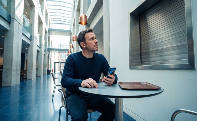 A person adult person sits in a bright civic café atrium as an unresolved credit card chargeback vs refund timeline interrupts an ordinary purchase decision.