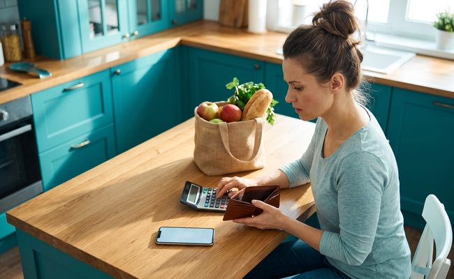 A person adult person weighs a hardship plan vs debt settlement decision while comparing a calculator and empty wallet in a bright apartment kitchen.