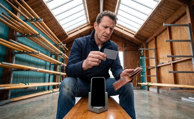 A person adult person moves a plain card toward a wallet while deciding whether to close a credit card after payoff in a rowing-club boathouse.