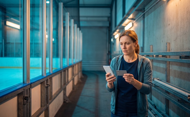 A person protects household cash in a bright ice-rink corridor while checking how autopay interacts with a plan to pay before the statement closes.