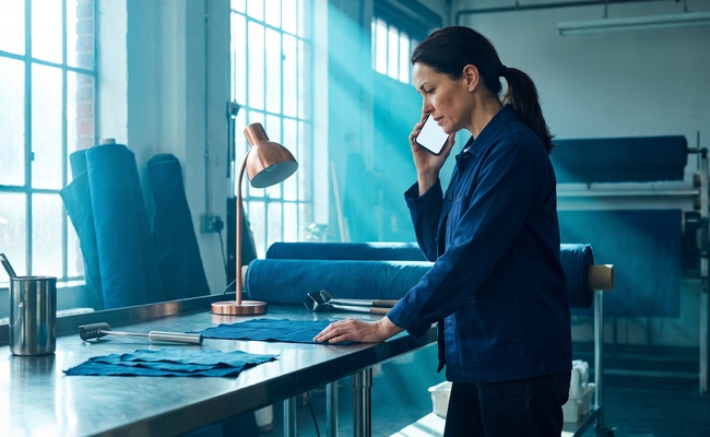 A person prepares an issuer refund request with a blank phone in a bright textile-dye studio after a credit card overpayment.