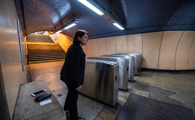 A person adult person investigates a reversed credit card payment beside subway turnstiles with a blank phone and closed wallet.