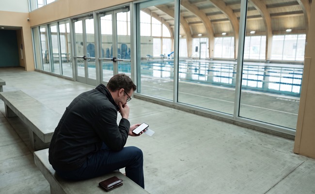 A person adult person compares account records for a reversed credit card payment at an aquatic-center entrance using a blank phone and plain card.
