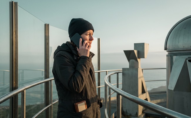 A person adult person makes a careful call about a pending credit card payment near a due date on a coastal observatory deck.