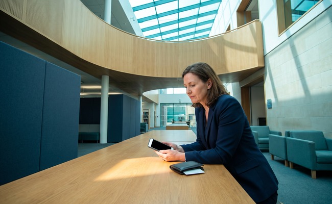 A person adult person in a university library atrium studies a blank phone while clarifying her credit card posting time.