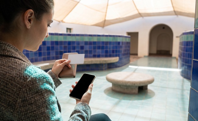 A younger adult person in a ceramic arts courtyard checks evidence before relying on her credit card posting time.