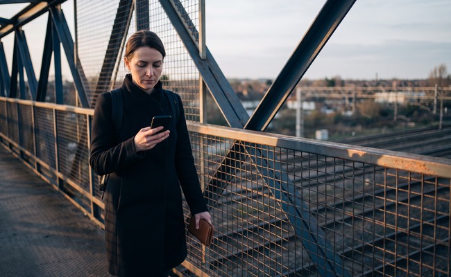 A person adult person on a suburban rail footbridge verifies confirmation details before deciding what her credit card posting time means.