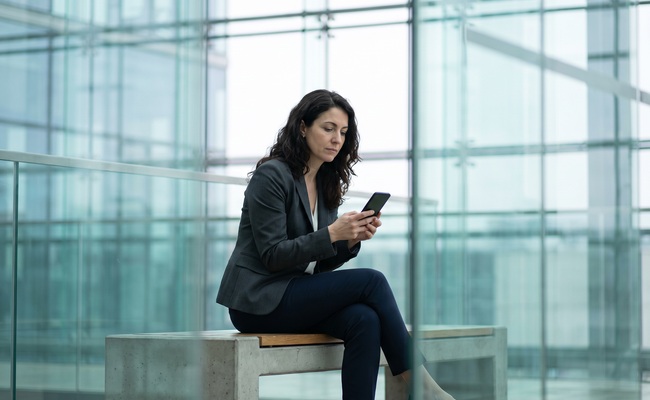 A person studies a blank phone while evaluating credit questions after a missed personal loan payment in a glass atrium.