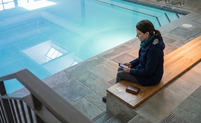 A person older adult person considers collection activity after a personal loan default on an aquatic-center viewing deck with a blank phone and closed wallet.