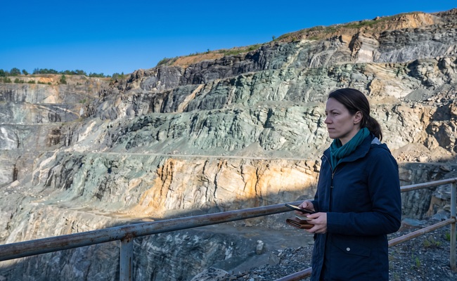 A person adult person evaluates a personal loan default payment decision at a stone-quarry overlook with a blank phone and closed wallet.