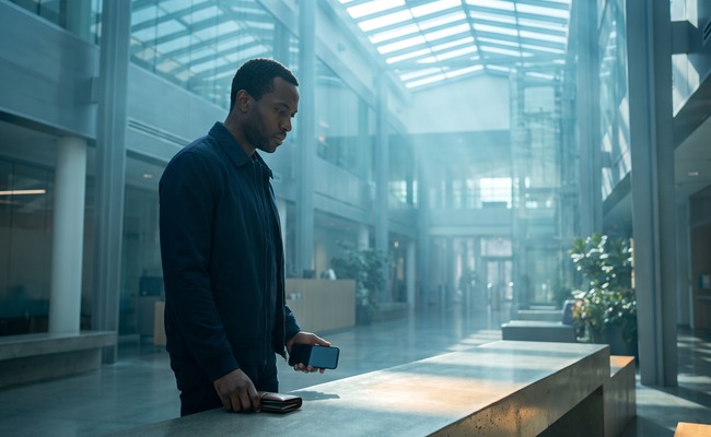 A person considers co signer loan risks in a bright science atrium while checking a blank phone beside a closed wallet.