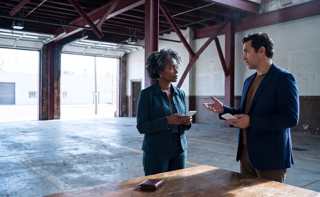 A person adult person discusses co signer loan risks with an adult adviser in an empty historic firehouse bay using blank phones.