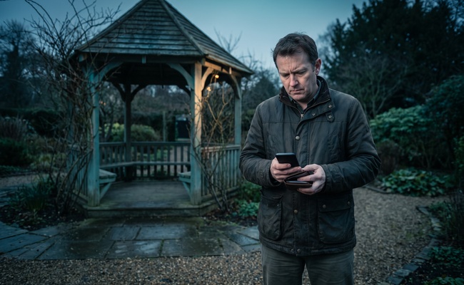 A person adult co-signer considers how to get released as a co signer beside a garden gazebo while checking a blank phone.