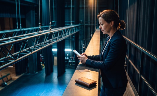 A person adult person verifies payment instructions before she pays off personal loan early above a public theater stage.