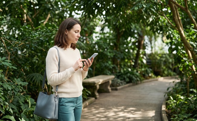 an adult person in her late 30s considers how to refinance a personal loan in a indoor botanical walkway with a curving path and dense green canopy.