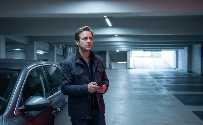 an adult person in his late 50s considers how to refinance a personal loan in a clean underground parking ramp with broad concrete geometry and empty lanes.