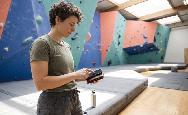 an adult nonbinary borrower in their early 30s considers how to refinance a personal loan in a indoor climbing gym with tall colored wall planes and open floor space.