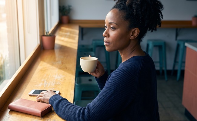 an adult person in her mid-40s considers how to refinance a personal loan in a quiet neighborhood café counter with an unbranded cup and open seating geometry.