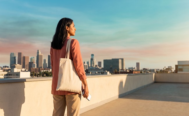an adult South person in her late 20s responds to car loan repossession warning signs in an open rooftop terrace with layered skyline, low parapet, and broad negative space.