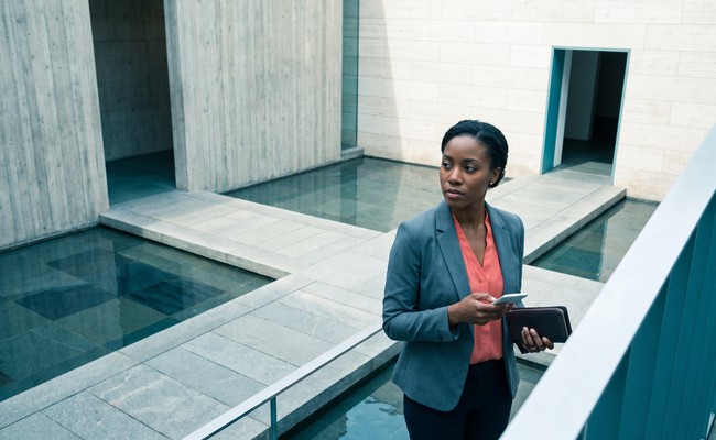 an adult person in her early 30s responds to what to do after car repossession in a quiet modern museum courtyard with tall walls, a shallow reflecting pool, and cross-axis paths.