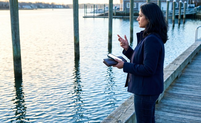 an adult South person in her early 40s responds to what to do after car repossession in a community boathouse dock with open water, vertical pilings, and a clear working edge.