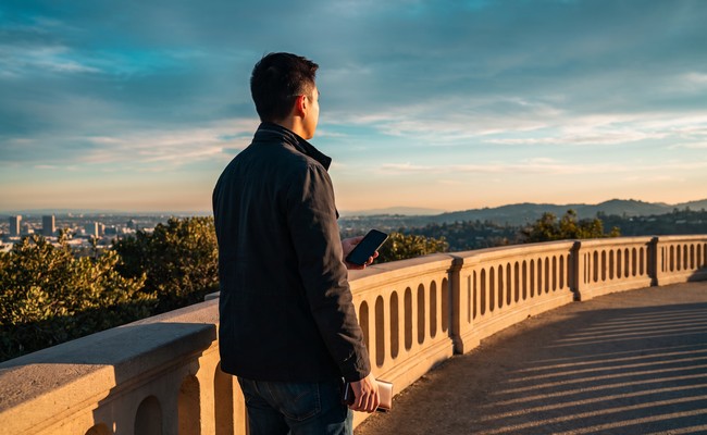 an adult person in his mid-20s responds to what to do after car repossession in a open observatory hill path with a curved guardrail, layered horizon, and broad sky.