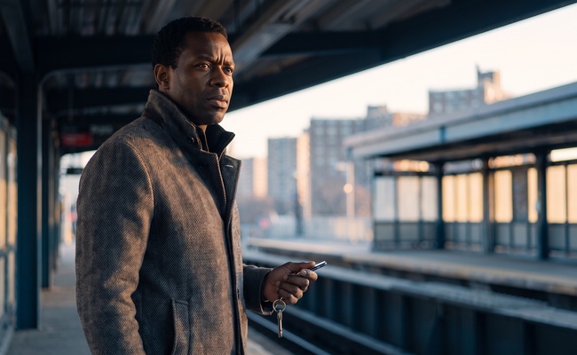 A person homeowner considers an FHA partial claim with keys and a blank phone at a covered train-platform plaza at dawn.
