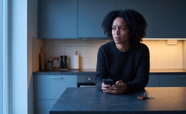 A person homeowner after alarming mortgage mail reviews next steps with a blank phone in a dawn kitchen.