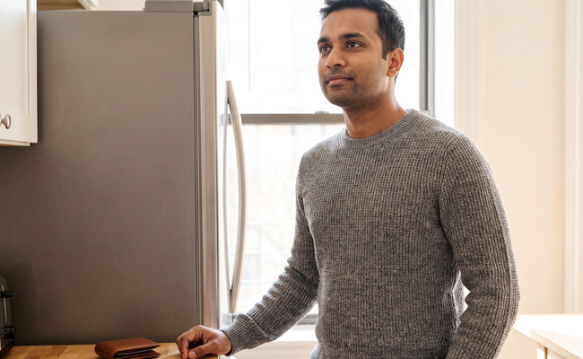 A person standing beside an unmarked refrigerator and considering household priorities