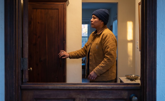 A person a distinct final review moment: an adult pauses in a quiet entryway beside a closed cabinet and visible carport, choosing the next safe action.