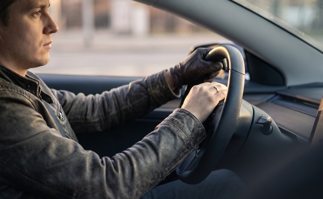 An adult rests both hands on a steering wheel in a parked car before making a phone call.